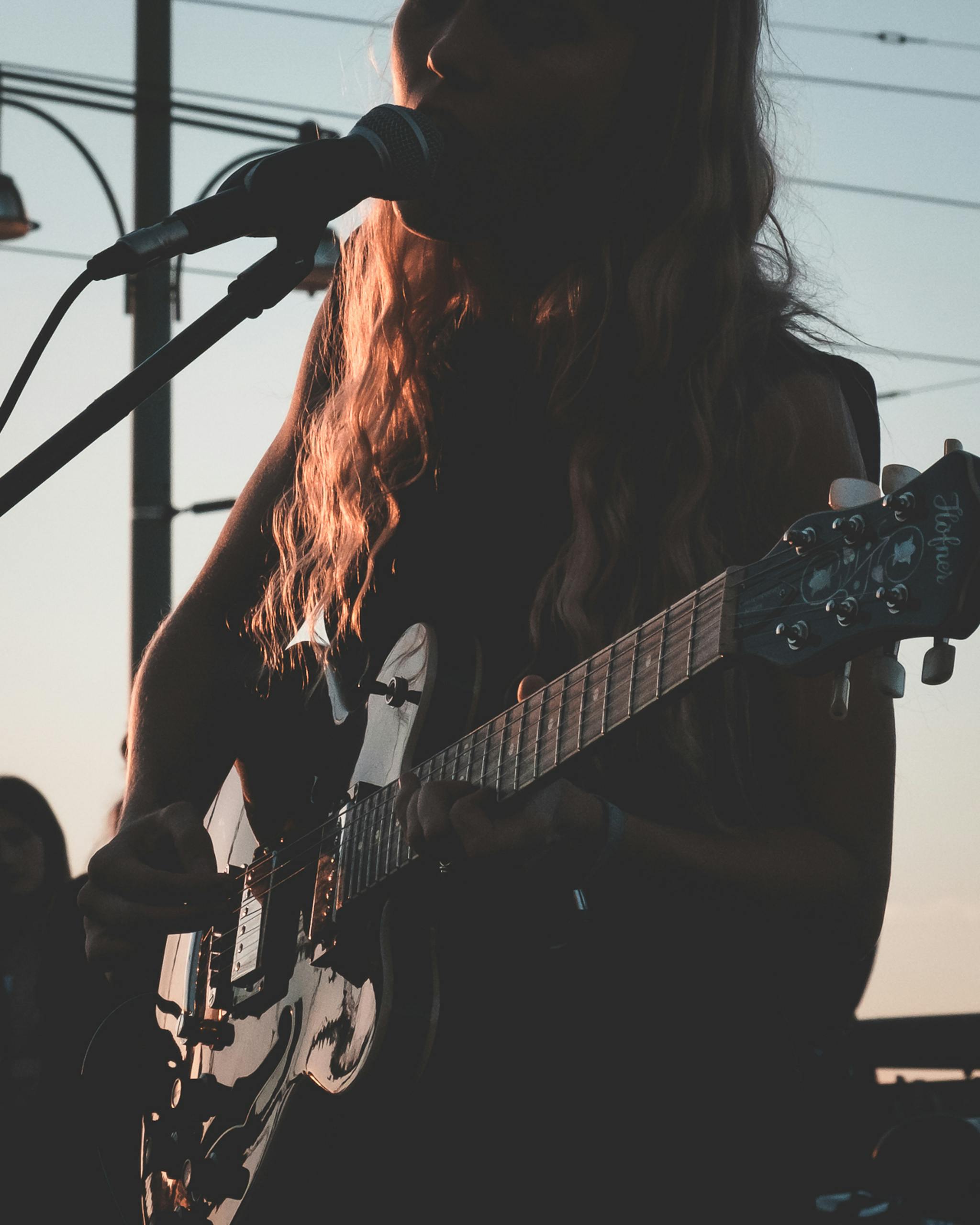 Crop unrecognizable female musician with wavy hair standing on stage and singing while playing electric guitar during concert